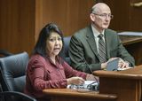 Sandra Skinaway sits at the testifiers' table and speaks to someone out of view. Representative Fischer sits next to her.